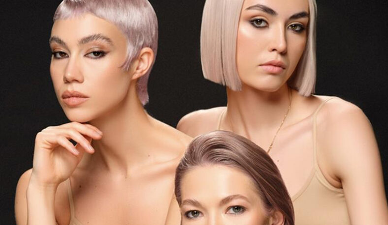 Tres mujeres con peinados cortos y colores rubio platino y rosa, maquillaje neutro y tops nude posan frente a un fondo negro en una imagen de estudio elegante pensada para profesionales.