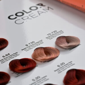 Muestrario profesional de colores de cabello mostrado en una carta brillante con mechones sedosos formando anillos en tonos cobre, rojizos y rosados para comparar acabados y elegir un tinte.