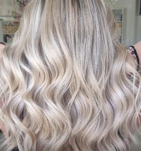 Vista posterior de cabello largo y ondulado en tonos rubios fríos y cálidos con mechas claras y oscuras, textura brillante y ondas suaves que muestran un acabado de alta calidad.