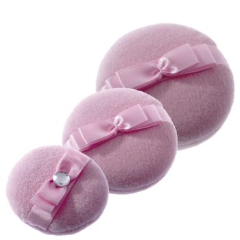 Tres almohadillas circulares de terciopelo rosa con lazos y una pedrería, en tres tamaños, presentadas como esponjas de polvos para maquillaje y peluquería.