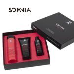 Estuche de regalo negro con interior rosa que muestra tres productos para el cuidado del cabello (una botella, un tubo y un dosificador) con el logotipo visible, presentado de forma elegante y apto para uso profesional.