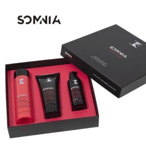 Estuche de regalo negro con interior rosa que muestra tres productos para el cuidado del cabello (una botella, un tubo y un dosificador) con el logotipo visible, presentado de forma elegante y apto para uso profesional.