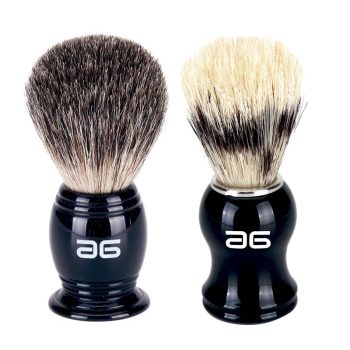 Dos brochas de afeitar colocadas sobre fondo blanco con mangos negros brillantes y cerdas densas —una de tonos gris oscuro y otra bicolor crema y negro—, diseño ergonómico y acabado alta calidad, verificado.