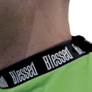 Primer plano del cuello y hombro de una persona con camiseta verde y ribete negro que repite la palabra Blessed en blanco, descripción accesible y profesional.