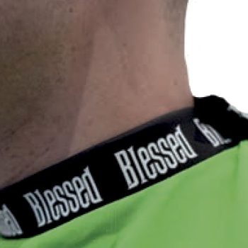 Primer plano del cuello y hombro de una persona con camiseta verde y ribete negro que repite la palabra Blessed en blanco, descripción accesible y profesional.