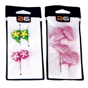 Dos tarjetas de exhibición con accesorios para el cabello: a la izquierda dos pares de pasadores con flores verdes/amarillas y rosas, a la derecha tres coleteros con corazones rosas con lunares, todo presentado en blister blanco con borde negro, apariencia de alta calidad y acabado profesional.