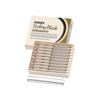 Caja abierta con bandeja de varias cuchillas dentadas para corte y peinado colocadas ordenadamente y una cuchilla suelta en primer plano, destinadas a uso en peluquería.