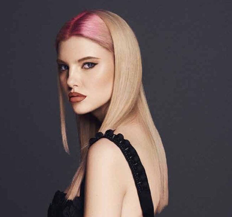 Retrato en primer plano de una mujer de piel clara con cabello largo y lacio rubio con raíces rosadas, maquillaje marcado con delineado de ojos y labios color terracota, mirada lateral y vestido negro, fotografía de alta calidad.