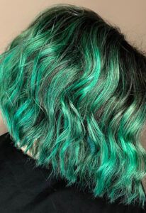 Cabello corto ondulado visto de perfil con raíces oscuras y reflejos verde esmeralda vibrantes en contraste sobre fondo neutro, fotografía de 'alta calidad'.