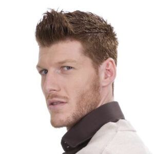 Hombre joven de perfil con barba corta y cabello castaño peinado hacia arriba, mirando por encima del hombro con expresión seria y aspecto profesional.