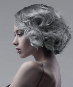 Retrato en blanco y negro de una mujer vista de perfil con cabello corto y ondulado, piel clara, maquillaje suave y hombros descubiertos sobre fondo neutro, imagen de alta calidad.
