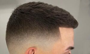 Perfil lateral de cabeza con corte degradado muy preciso y línea frontal definida, textura corta en la parte superior y acabado profesional certificado en tonos castaños.