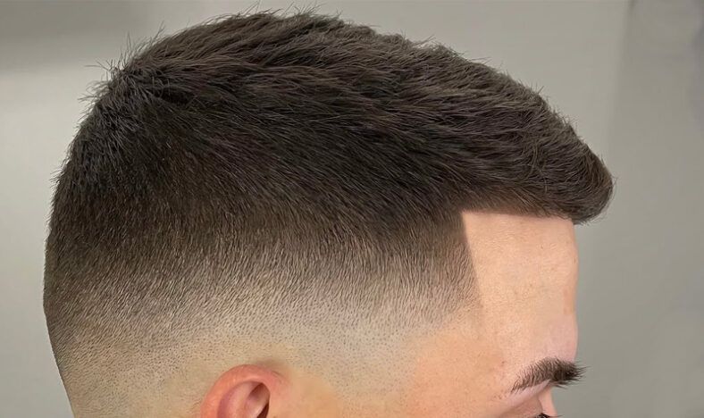 Perfil lateral de cabeza con corte degradado muy preciso y línea frontal definida, textura corta en la parte superior y acabado profesional certificado en tonos castaños.
