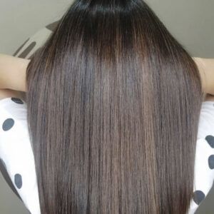 Cabello largo, liso y brillante de tono castaño oscuro visto desde atrás sobre una camiseta blanca con lunares negros, con un acabado 'profesional'.