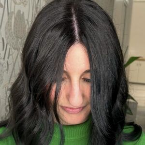 Persona de cabello largo y oscuro con raya al medio mirando hacia abajo y con suéter verde en un interior, retrato de alta calidad.