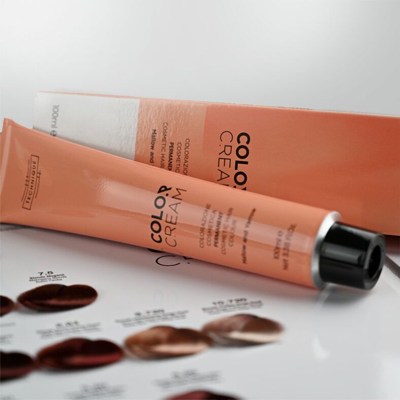 Tubo y estuche de crema colorante en tono melocotón dispuestos sobre una carta de muestras de tonos de cabello, con empaque brillante de alta calidad y aspecto comprobado.