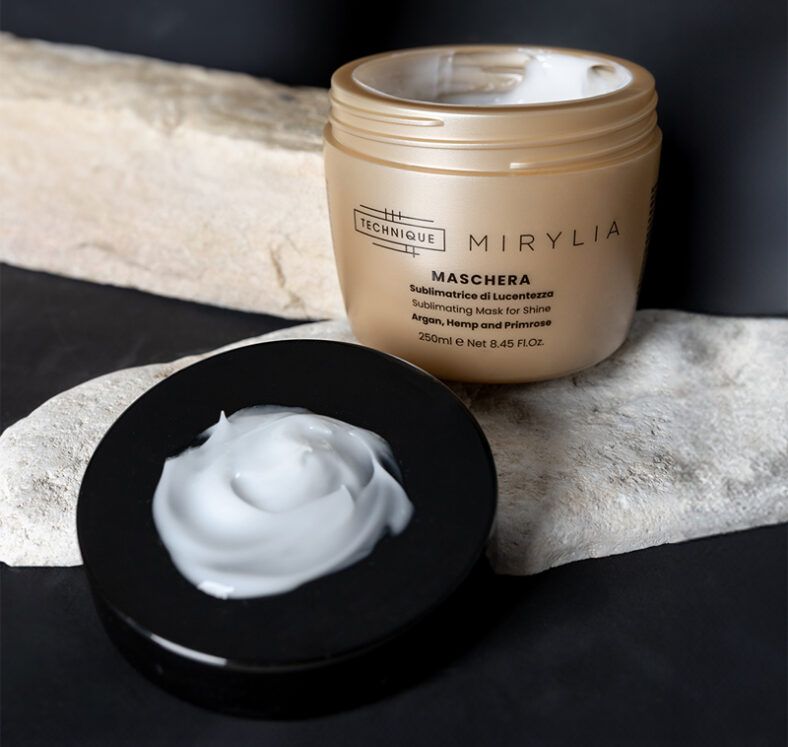 Envase dorado abierto de mascarilla capilar junto a su tapa negra con crema blanca sobre una piedra clara y fondo oscuro, presentación elegante que transmite 'alta calidad'.