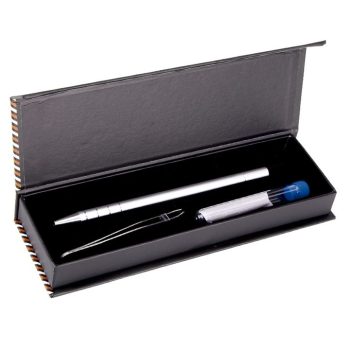 Estuche negro abierto con interior acolchado que contiene una herramienta metálica plateada tipo bolígrafo, unas pinzas de precisión y un pequeño tubo con tapa azul sobre fondo blanco (peluquería).