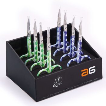 Juego de pequeñas tijeras de precisión con mangos estampados a cuadros en tonos verdes y azules colocadas en un expositor negro, diseñadas para trabajos cosméticos y de detalle y de alta calidad.