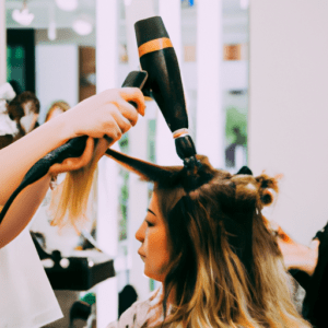 Cliente sentada en un salón mientras una estilista usa secador y cepillo redondo para peinar un mechón de cabello con mechas rubias, mostrando un entorno profesional y herramientas de alta calidad.