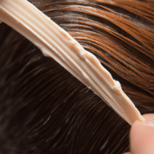 Mano aplicando un producto capilar cremoso sobre un mechón de cabello castaño oscuro húmedo, mostrando textura y brillo de alta calidad.