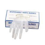 Caja blanca con borde azul de guantes desechables de vinilo y un guante transparente colocado sobre la abertura de la caja con texto azul visible en la tapa, 'peluquería'.